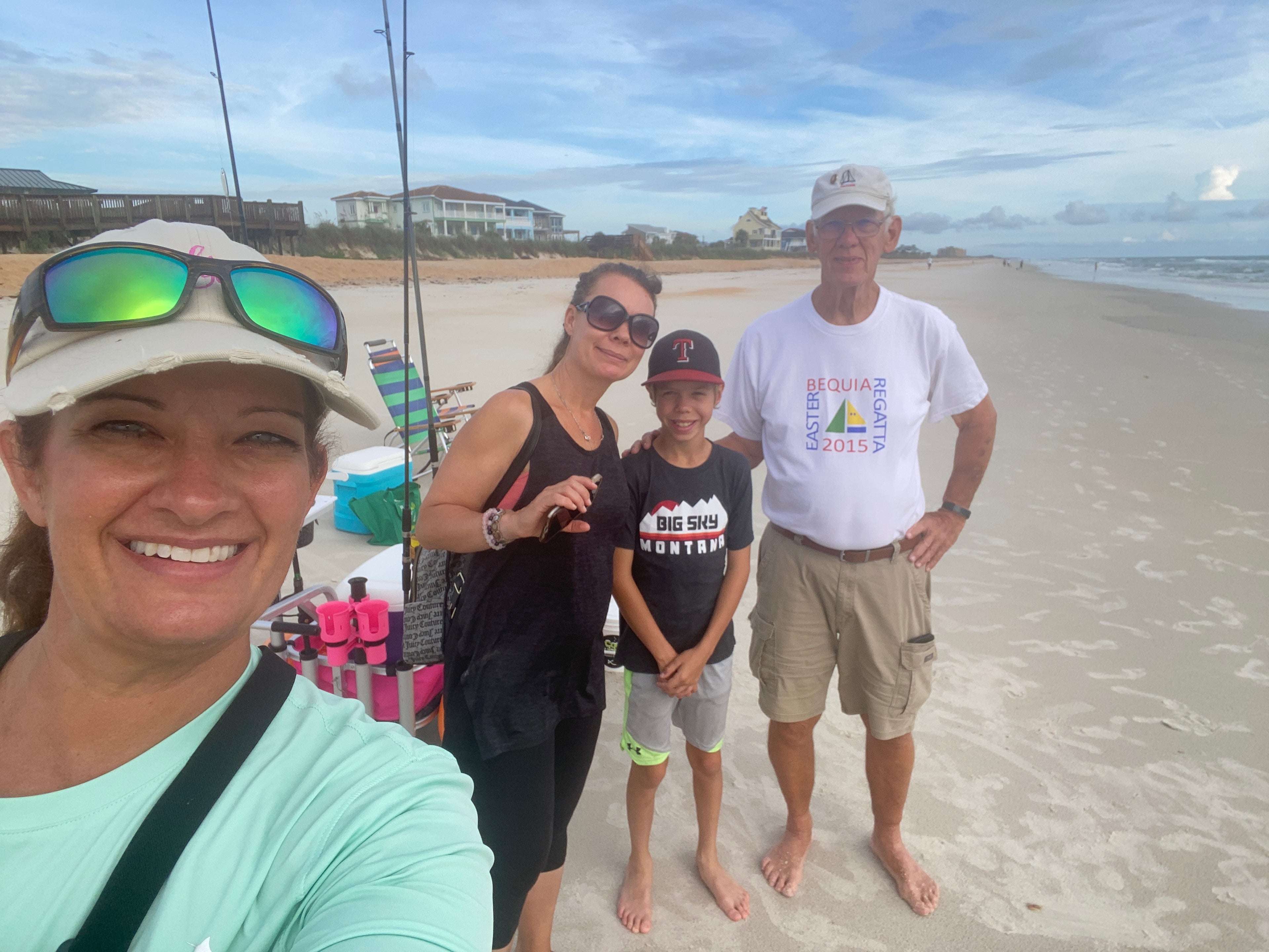 Cathy Sanders talking a selfie with some surf fishing charter clients on a beach. The pink Fishin' Girl cart is behind them. 