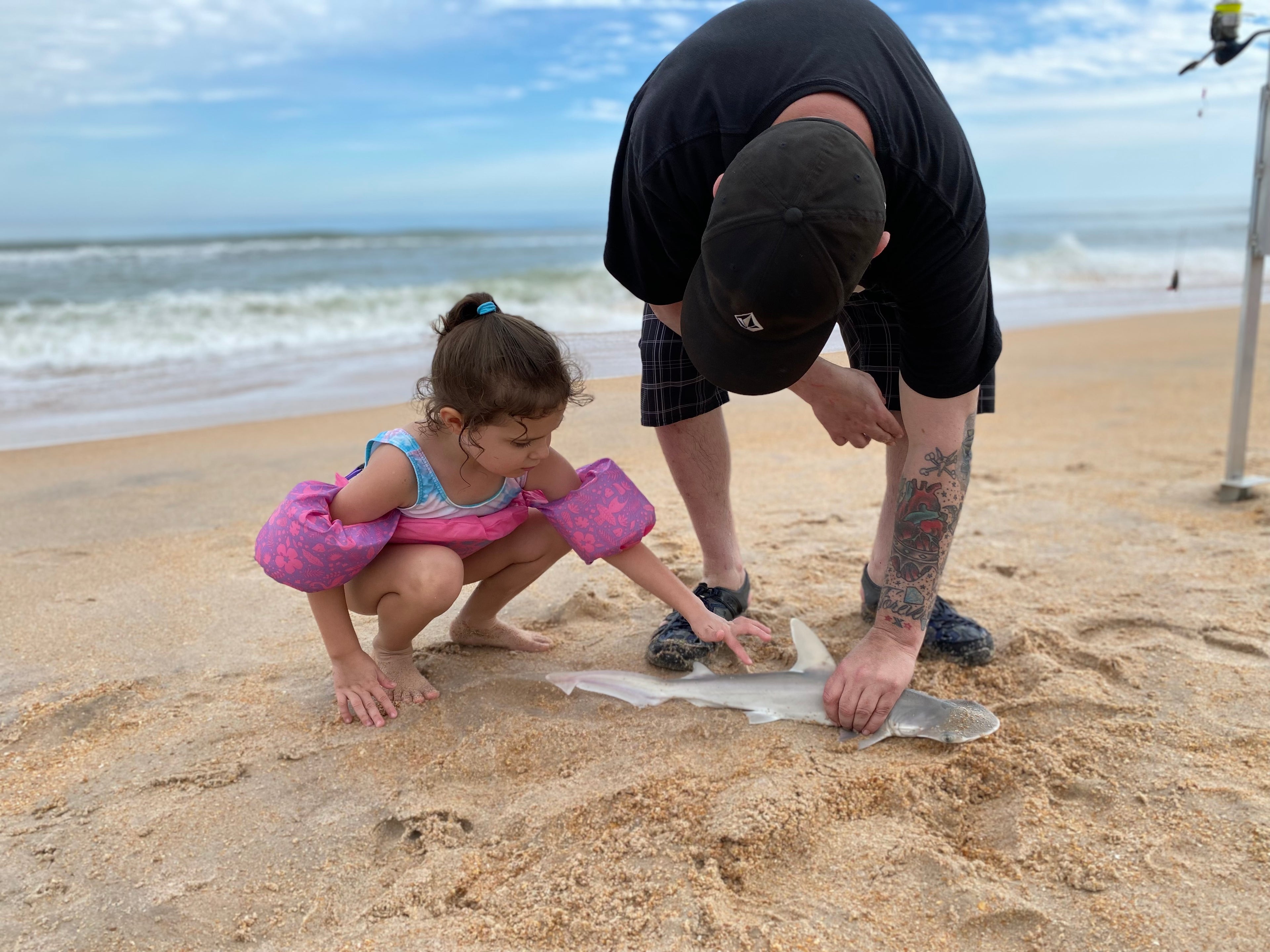 One of our charter clients holding a small shark secure on the sand while his daughter touches a finger on the shark's back